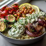 A freshly prepared Mediterranean Buddha Bowl garnished with parsley and lemon wedges, featuring chickpeas, creamy Greek yogurt, and roasted veggies.