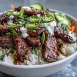 A vibrant Korean Beef Power Bowl with sesame-ginger beef, fluffy rice, tangy pickled carrots, and creamy sriracha mayo.