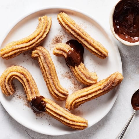 A hand dips a warm churro into dark chocolate ganache, drizzling with powdered sugar.