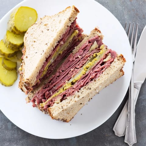 A close-up of a Pastrami on Rye sandwich with sharp mustard and pickles, perfect for a quick lunch or dinner.