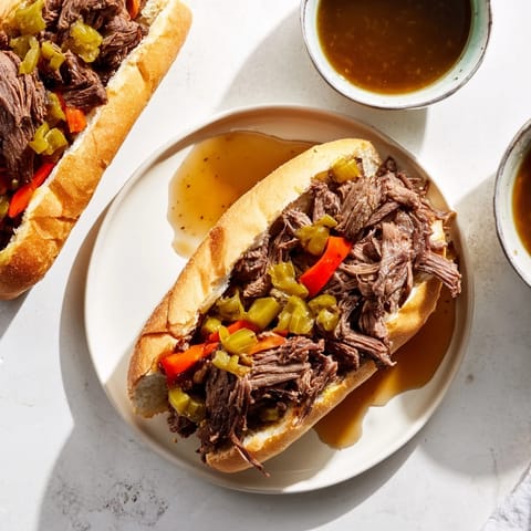 A plated Italian Beef Sandwich overflowing with juicy shredded beef, tangy giardiniera, and roasted peppers on a toasted roll.