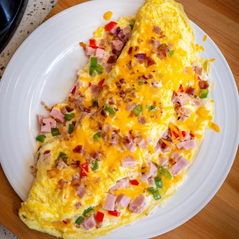A fluffy Denver Omelet oozing melted cheddar cheese, served alongside crispy hash browns and buttered toast on a rustic table.