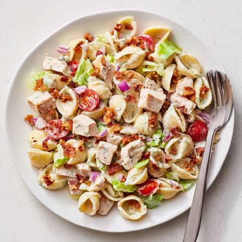 A plated serving of BLT Chicken Pasta Salad with tender pasta shells, grilled chicken, crisp romaine, and cherry tomatoes topped with crumbled bacon.  