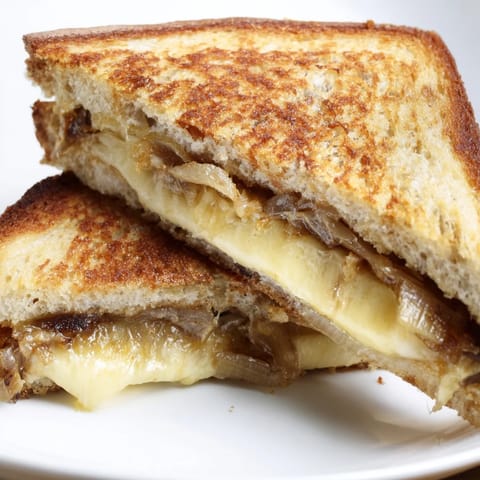 A close-up of a golden-brown Caramelized Onion & Gruyère Gratty Grilled Cheese sandwich, showcasing melted, nutty Gruyère cheese and sweet, slow-cooked caramelized onions on crispy country bread.