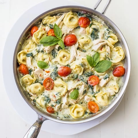 Fork twirls tender cheese tortellini coated in creamy pesto sauce, served hot from the skillet with fresh basil garnish.