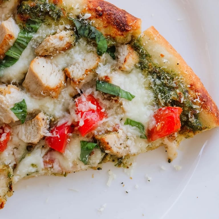 A rustic homemade Chicken Pesto Pizza emerges from the oven, featuring a golden crust topped with chicken, pesto, and tomatoes.