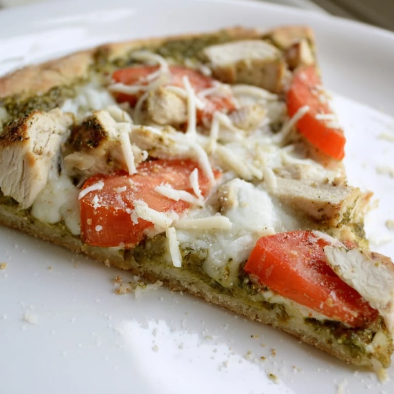 Savory diced chicken and basil pesto are spread evenly over a thin crust with mozzarella and tomato slices.