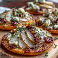 Freshly baked Pear, Gorgonzola, and Pickled Walnut Pizzettes topped with honey and arugula on a rustic wooden board.